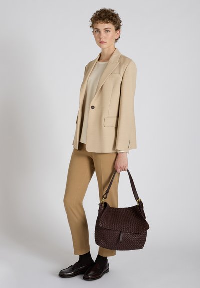 Beige taillierter Blazer, passende Hose, cremefarbenes Oberteil, dunkle geflochtene Handtasche und polierte braune Loafers. Glatte Textur, strukturierte Passform, schlichtes Design.