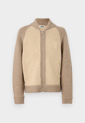 Strik cardigan i beige nuancer med lynlåsåbning, ribbede ærmer og kontrastteksturer samt en lille logo-detail på brystet.
