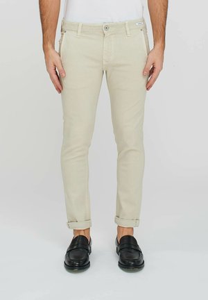 Pantaloni beige slim-fit realizzati in un tessuto misto cotone, con tasche frontali e maniche arrotolate. Abbinati a mocassini neri.