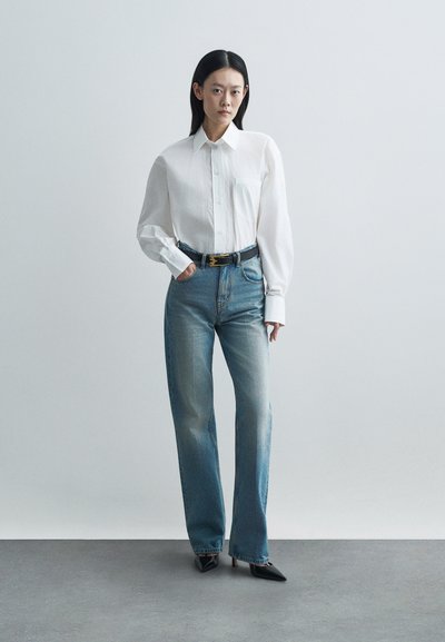 Λευκό πουκάμισο με μακρύ μανίκι και τσέπη στο στήθος, σε συνδυασμό με ελαφριά μπλε tapered τζιν και μαύρες γόβες με μυτερή μύτη.