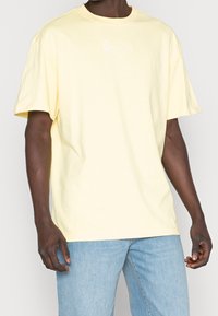 Gul bomull T-shirt med kort ärm, rund hals och en vit logotyp på bröstet. Lös passform med en mjuk, slät struktur.