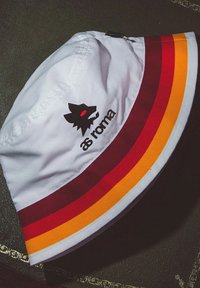Witte bucket hat met rode, kastanjebruine en oranje strepen. Zwarte wolf logo met rode ogen en "as roma" tekst aan de voorkant. Zacht materiaal.