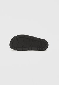 Suola di scarpa in gomma nera con grip testurizzato, caratterizzata da un design del battistrada a motivi e sezioni rialzate per una migliore trazione e durata.