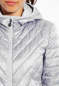 Jasnoszara ocieplana kurtka z wzorem w jodełkę, pełnym zamkiem błyskawicznym i kapturem. Charakteryzuje się subtelnym brandingiem i gładką, błyszczącą fakturą.