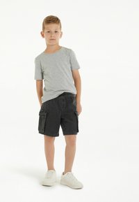 Šedé bavlněné tričko, černé džínové cargo šortky s bočními kapsami a bílé tenisky. Neformální outfit s uvolněným střihem a elastickým pasem.