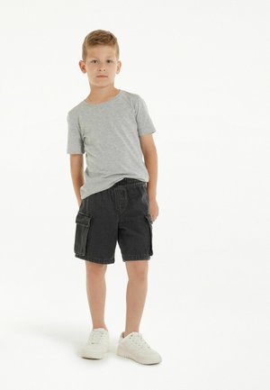 T-shirt en coton gris, shorts cargo en denim noir avec poches latérales, et baskets blanches. Tenue décontractée avec une coupe ample et une taille élastique.