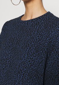 Blauwe trui met een gestructureerd luipaardprintpatroon in het zwart. Ronde halslijn met een gebreide afwerking. Minimalistisch ontwerp, korte mouwen.