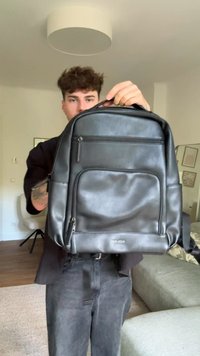 Černý kožený batoh s několika zipovými kapsami, hladkým povrchem a ergonomickým tvarem. Obsahuje horní uchopovací rukojeť a nastavitelné popruhy.