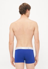 Blaue Baumwoll-Boxershorts mit einem weißen Bund, der ein rotes und blaues Logo zeigt. Der Stoff wirkt glatt und der Schnitt ist enganliegend.