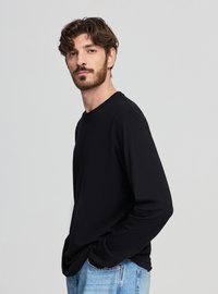 Maglietta nera a maniche lunghe realizzata in materiale morbido, con scollo rotondo e taglio rilassato, abbinata a jeans di denim azzurro chiaro.