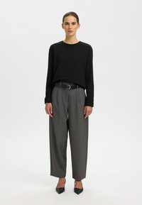 Zwart shirt met lange mouwen, grijze geruite broek met brede pijpen en zwart pumps met spitse neus. Riem met zilveren gespsdetails.