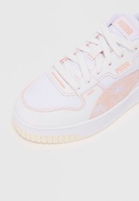 White sneakers with light pink accents, smooth leather and textured mesh, featuring a rubber sole and the Puma logo.