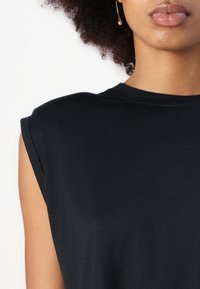 Top negro sin mangas con cuello redondo, hecho de una tela suave. Presenta detalles de costura sutiles y un corte relajado.