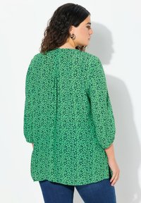 Blusa verde con motivo floreale nero, maniche a tre quarti, scollatura rotonda e vestibilità morbida. Caratterizzata da un orlo asimmetrico e una texture di tessuto morbida.
