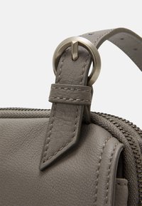 Szczegół szarej skórzanej torby z metalową klamrą, starannym szwem i teksturowaną powierzchnią w pobliżu zamka błyskawicznego.