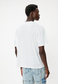 Vit bomull t-shirt med en avslappnad passform, korta ärmar och rund halsringning. Bakom har den en enkel design utan synliga detaljer.
