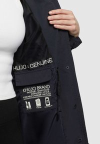 Námornícka bunda s sieťovinovou podšívkou a viacerými vnútornými vreckami označenými na pas, smartphone a doplnky. Disponuje nastaviteľnými šnúrkami.