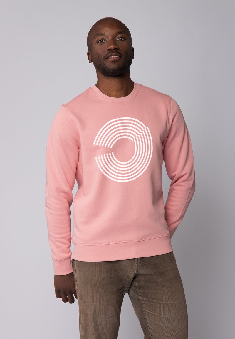 Lichtroze sweatshirt met een cirkelvormige witte lijn grafiek. Ronde hals, lange mouwen, geribbelde manchetten en zoom, gemaakt van zachte stof. Gecombineerd met bruine broek.