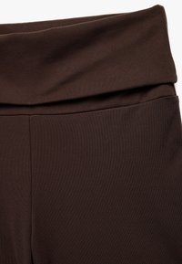 Close-up van donkergroene hoge taillebroek met een gevouwen tailleband en een gladde stof.