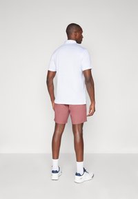 Hvit kortermet polo skjorte kombinert med lyserøde shorts, sett fra bak. Antrekket har en avslappet passform og enkel design.