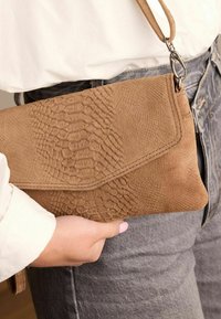 Tan gekleurde clutch tas met een slangenhuidpatroon, voorzien van een flapafsluiting en een polsband. Gemaakt van zacht materiaal.