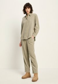 Woman wearing loose beige corduroy shirt and matching pants with tan platform ankle boots, standing against a plain light background.