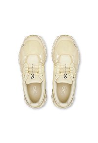 Zapatillas deportivas beige con parte superior de malla, cordones elásticos y suela acolchada. Marca "on" visible en los laterales y plantillas.