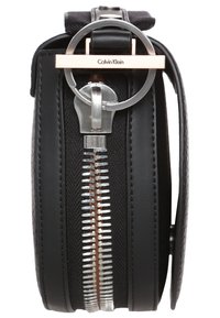 Czarna skórzana torba z okrągłym metalowym suwakiem i akcentem w kolorze różowego złota, posiadająca fakturowaną powierzchnię oraz wyrazisty wzór zamka błyskawicznego.