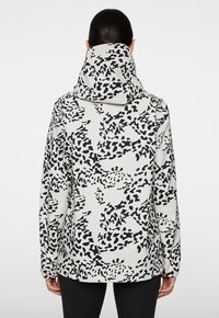 Kapturowa kurtka w biało-czarny wzór zwierzęcy, charakteryzująca się luźnym krojem, długimi rękawami i elastycznymi mankietami.