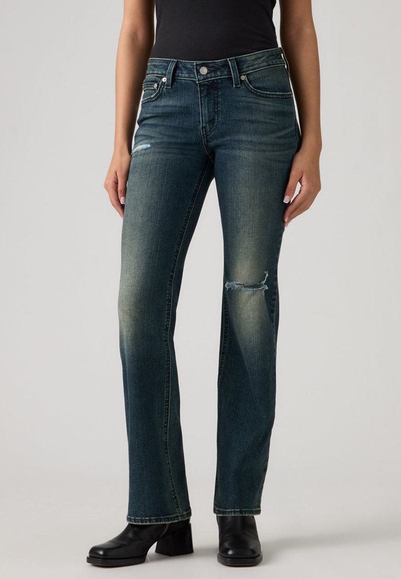 Jean en denim bleu foncé avec une coupe droite, présentant un genou usé, un léger délavage et un design classique à cinq poches.