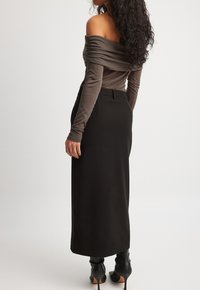 Off-the-shoulder, bruine top met gerimpelde textuur, gecombineerd met een lange zwarte rok. Heeft een aansluitende silhoutte en enkellange zwarte hakken.