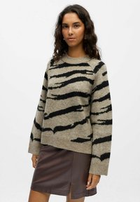 Gebreide trui met een beige en zwarte gestreepte patroon, ronde hals, en lange mouwen, gecombineerd met een bruine neplederen rok.