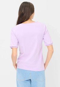 Lavendel kortærmet top med rund halsudskæring og kroget trim ved ærmerne. Glat tekstur, afslappet design, båret med lyseblå denimjeans.