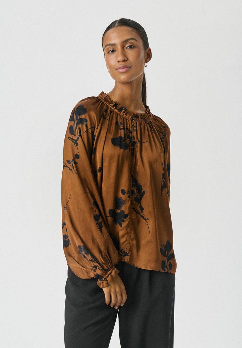 Bruine bloemenblouse met een gerimpelde halslijn, lange mouwen en knoopdetails aan de voorkant. Gladde stof met zwarte bloemenpatronen.