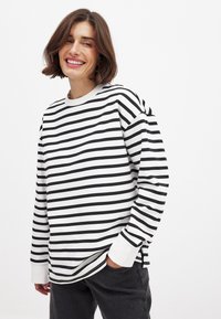 Črno-bela črtasta srajca z dolgimi rokavi in okroglim vratnim izrezom, ki ima rebraste manšete in sproščen kroj. Brez vidnih oznak blagovne znamke.