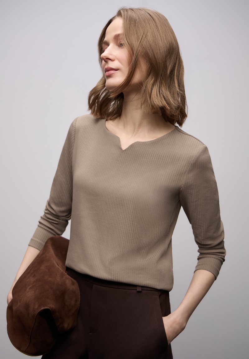 Beżowy prążkowany top z długim rękawem o subtelnym dekolcie w kształcie litery V, zestawiony z ciemnobrązowymi spodniami i brązową, fakturowaną kopertówką.