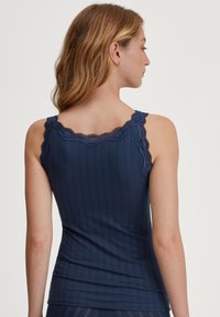 Marineblauw tanktop van ribstof, met een geschulpte kanten rand langs de halslijn en schouderbanden, in een aansluitende snit.