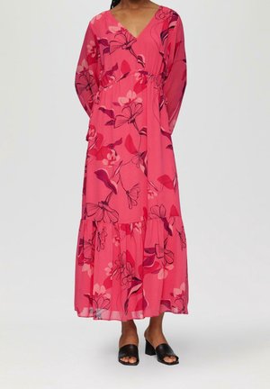 Nainen pukeutunut pitkään vaaleanpunaiseen kukkakuosiseen mekkoon, jossa on V-pääntie ja pitkät hihat, ja hänellä on jalassaan mustat avoimet varvassandaalit, joissa on leveä korko.