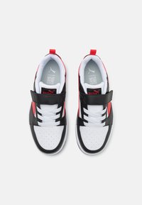 Des chaussures de sport noires, blanches et rouges avec une texture lisse, une zone de orteil perforée, deux lacets élastiques et une sangle en Velcro pour la fermeture.