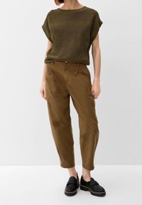 Olive green, textured knit top paired with brown, relaxed-fit trousers. Footwear features black, chunky loafers with a strap detail.