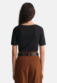 Sort kortærmet top med rund halsudskæring, parret med højttaljede brune bukser og et tekstureret sort bælte. Glat stoftekstur.