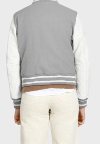 Gray and white bomber jacket with a ribbed collar, striped hem, and contrasting brown accents. Features leather and fabric materials.