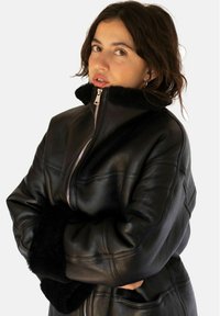 Zwarte leren jacket met een hoge kraag, ritssluiting aan de voorkant en zachte, bontachtige manchetten. Kenmerkt zich door gestikte panelen en een ontspannen pasvorm.