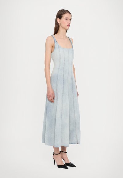 Hellblaues Jeanskleid mit tailliertem Oberteil, quadratischem Ausschnitt und ausgestellt Rock. Kombiniert mit schwarzen spitzen Absätzen und Knöchelriemen.