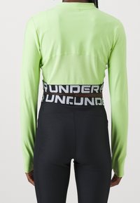 Langärmliges, leuchtend grünes Oberteil mit geripptem Muster und einem Netzpaneel am Rücken. Schwarze, hochtaillierte Leggings mit kontrastierendem weißen Schriftzug am Bund.