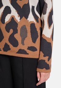 Knit sweater featuring a brown, black, and cream leopard print design, with a soft texture and long sleeves. Black pants are partially visible.