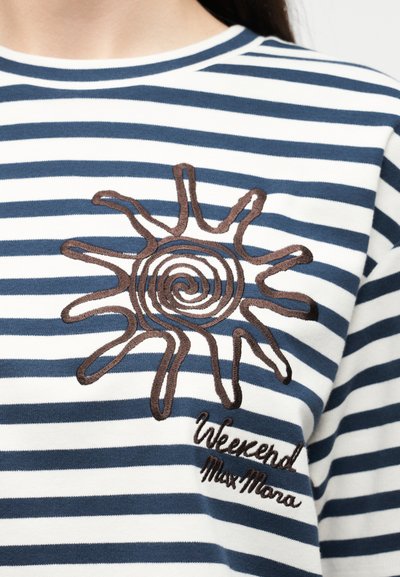 Κοντινό πλάνο πουκάμισου με ναυτικό μπλε και άσπρες ρίγες, διακοσμημένο με καφέ κέντημα ήλιου και την επιγραφή "Weekend Max Mara" στο στήθος.