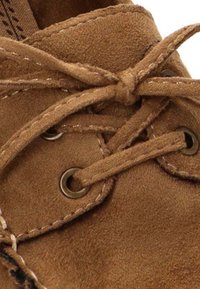 Zapato de gamuza marrón con cordones redondos, ojales de metal y detalles de costura. La vista en primer plano resalta la textura y la configuración de los cordones.