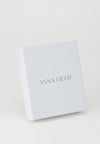 Baltas stačiakampis dovanų dėžutė su lygiu paviršiumi, ant kurios priekinės pusės yra ‚ANNA FIELD‘ logotipas paprastu sans-serif šriftu pilkos spalvos.