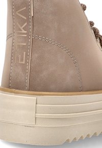 Bota de ante marrón con tacón, detalle de costura y suela de goma beige estriada, que presenta el nombre de la marca "ETNIKL" en el panel lateral.